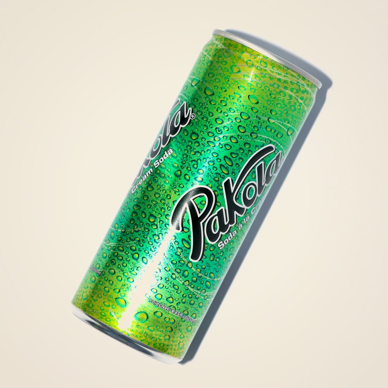 A green can of Pakola ice-cream soda, beaded with condensation, against a warm cream background.