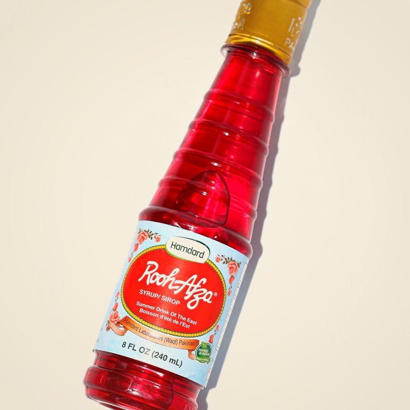 A bottle of Hamdard Rooh Afza, a crimson rose-and-herb syrup, against a warm cream background.